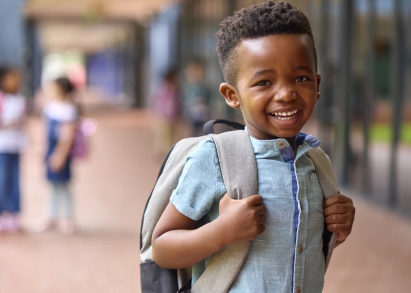 Portrait d'un élève souriant d'école primaire, sac à dos à l'extérieur, à l'école
